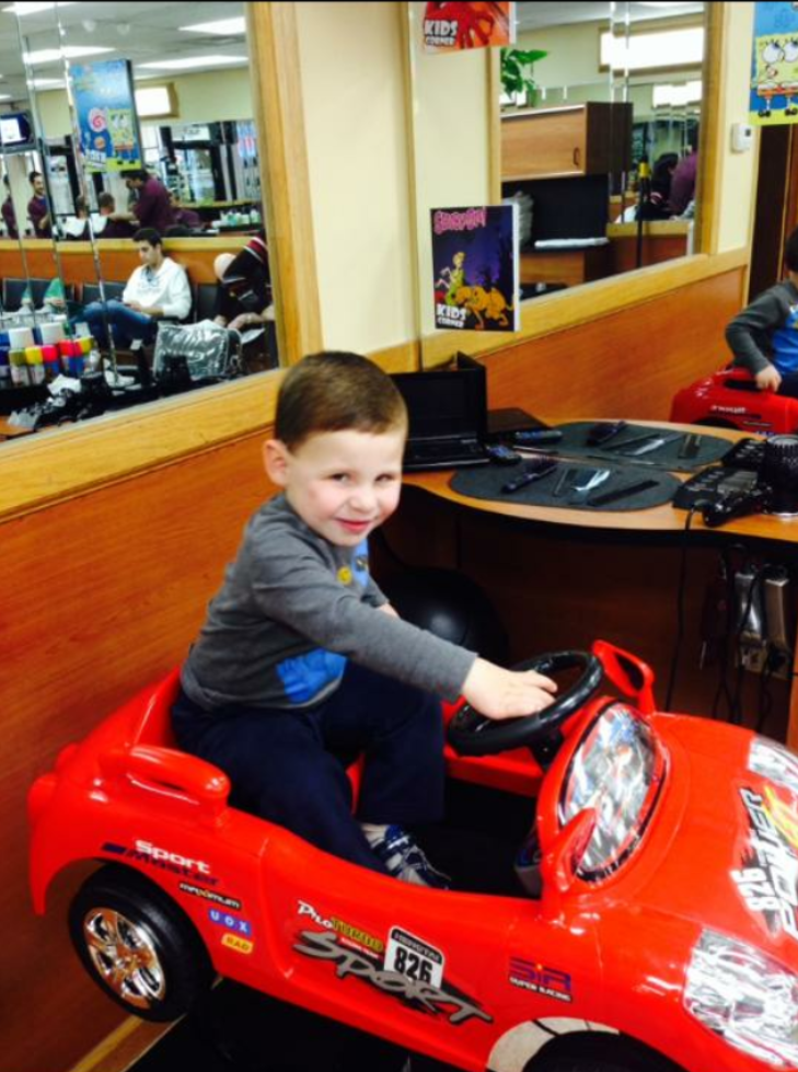 Child seated in a red car-shaped barber chair at Jacob's Barber Shop